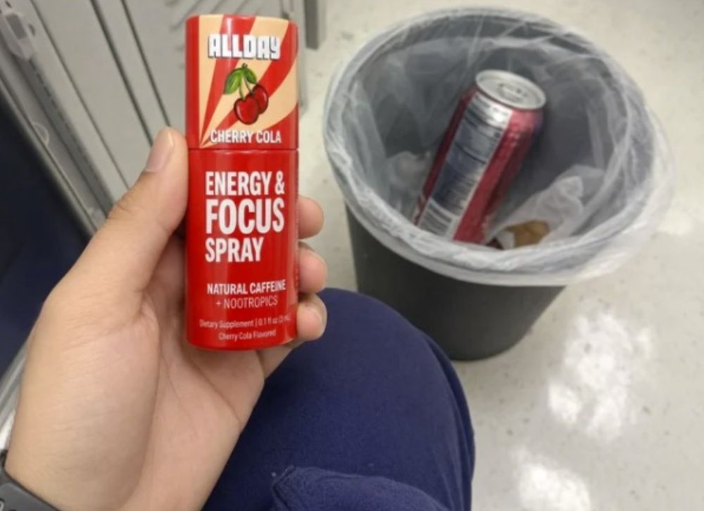 Hand holding AllDay over a bin with an energy drink can